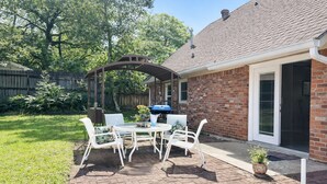 Eine Terrasse mit Tisch und Stühlen, ein Grill und ein Ziegelhaus mit überdachter Terrasse.