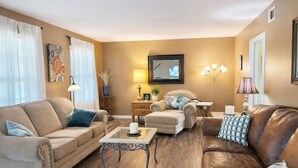 Ein Wohnzimmer mit einem beigen Sofa, einem braunen Ledersofa, einem Glastisch und einem Beistelltisch mit einer Lampe.