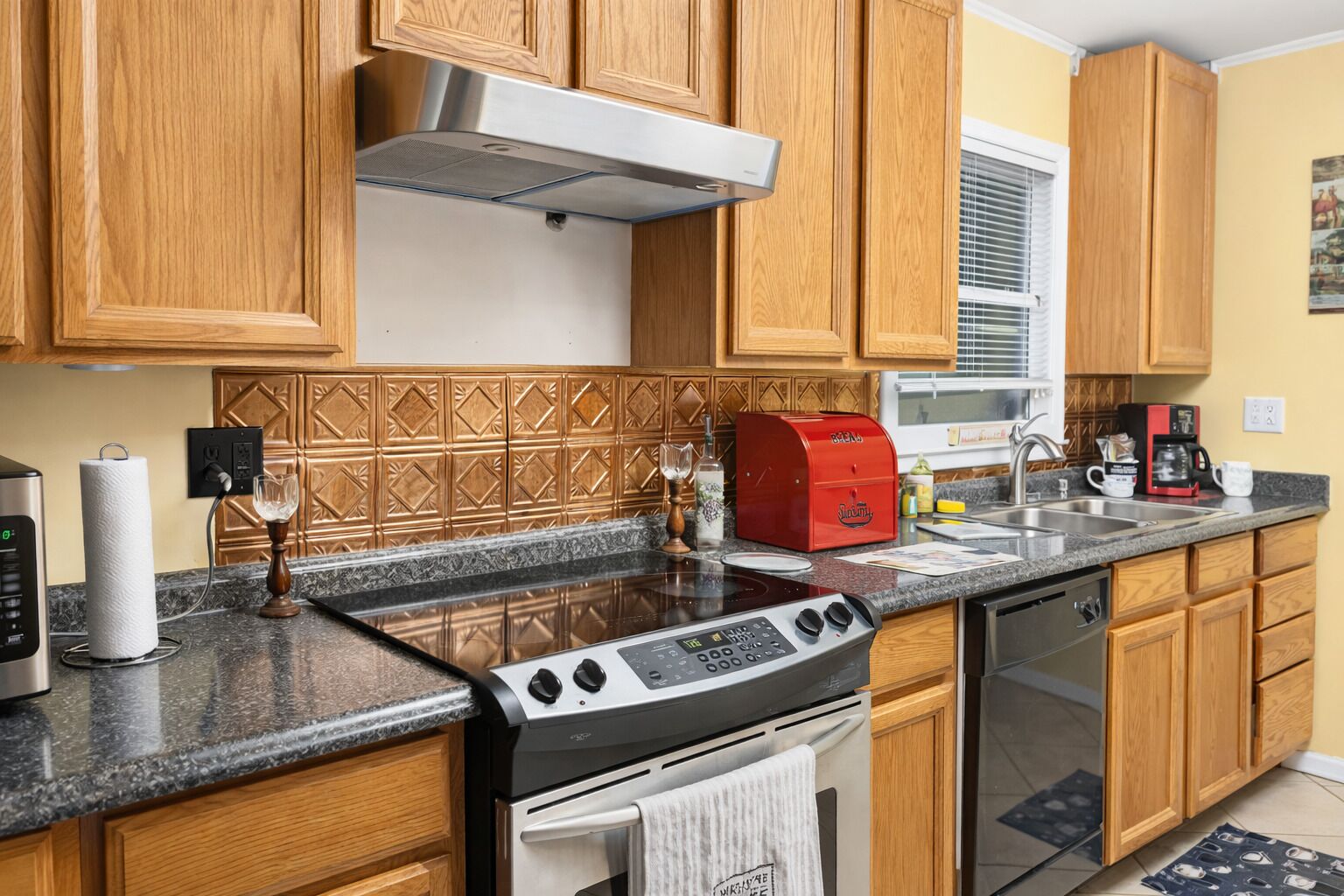 A kitchen with wooden cabinets, a stainless steel range hood, a red toaster, and a dishwasher.