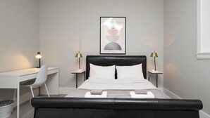 A modern bedroom with a black headboard, white bedding, a desk, and two bedside lamps. - Modern Comfort 2BR in Delta - Near Parks & Shops (Delta)