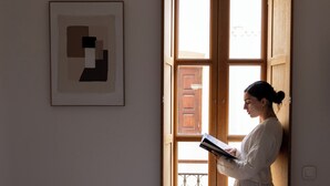 Een kamer met een bed, een raam met houten luiken en een lijst met abstracte kunst aan de muur.