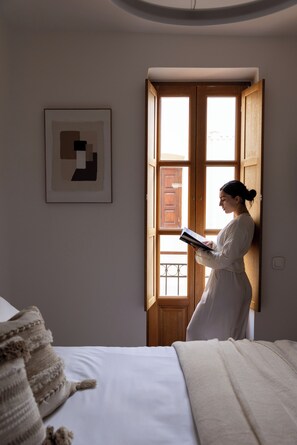 Ein Zimmer mit einem Bett, einem Fenster mit Holzläden und einem gerahmten abstrakten Kunstwerk an der Wand.
