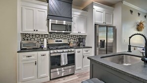 A modern kitchen with white cabinetry, stainless steel appliances, a patterned backsplash, and a built-in island with a sink. - Bright Amarillo Townhome with Yard and Garage (Amarillo)