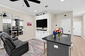 A modern living room with a black leather sofa, a flat-screen TV, and a kitchen area with white cabinets and a microwave. - Bright Amarillo Townhome with Yard and Garage (Amarillo)