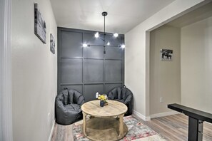 Een kamer met een donkere wandpaneel, een ronde houten tafel met een vaas, twee zwarte relaxfauteuils, en een plafondlamp.