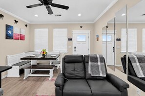 Ein modernes Wohnzimmer mit einer schwarzen Ledersofa, einem Esstisch mit weißen Stühlen und einem Deckenventilator.