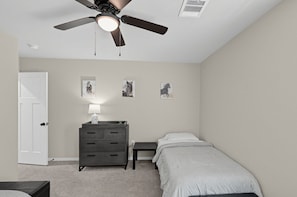 Ein Schlafzimmer mit einem Bett, einem Schminktisch, einem Deckenventilator und Wandbildern.