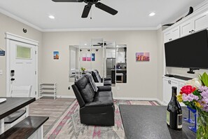 A modern living room with a black leather sofa, a flat-screen TV, and a dining area with a bench and table. - Bright Amarillo Townhome with Yard and Garage (Amarillo)