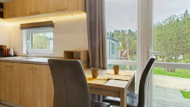 A modern kitchen with wooden cabinets, a window, and a dining area with a table and chairs.