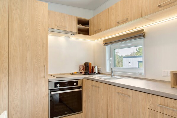 A modern kitchen with wooden cabinets, a built-in oven, a window, and a countertop.