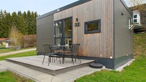 A modern building with a wooden facade, a number '32' sign, and a patio with outdoor furniture.