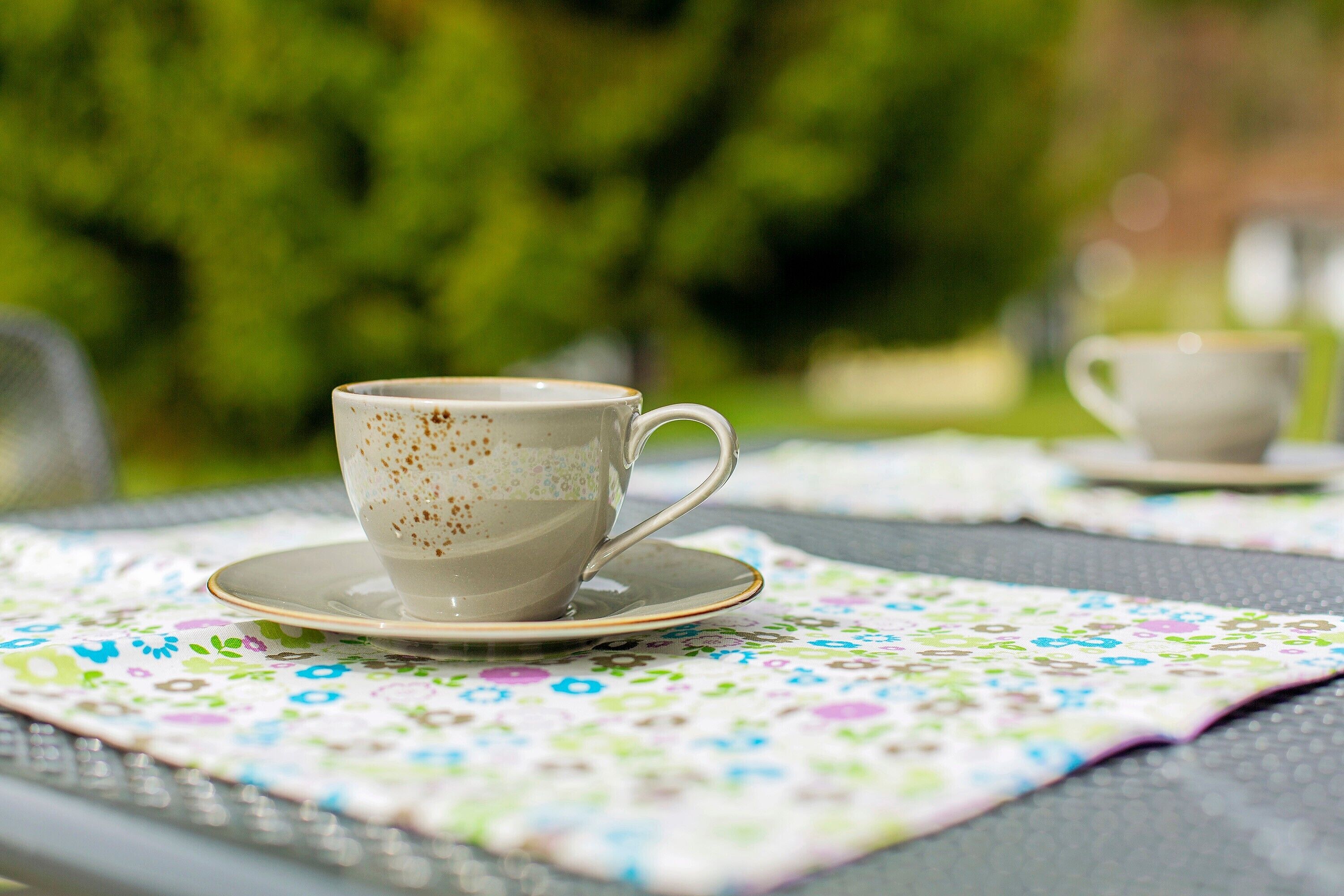 A cup of coffee on a table with a floral placemat.