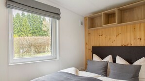 A bedroom with a large window, a bed with grey bedding, and a wooden headboard.