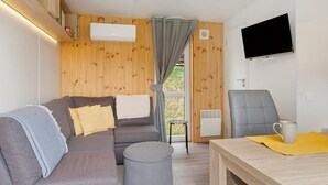 A modern room with a grey sofa, a small round ottoman, a wooden table with a yellow placemat, a grey chair, and a mounted TV.