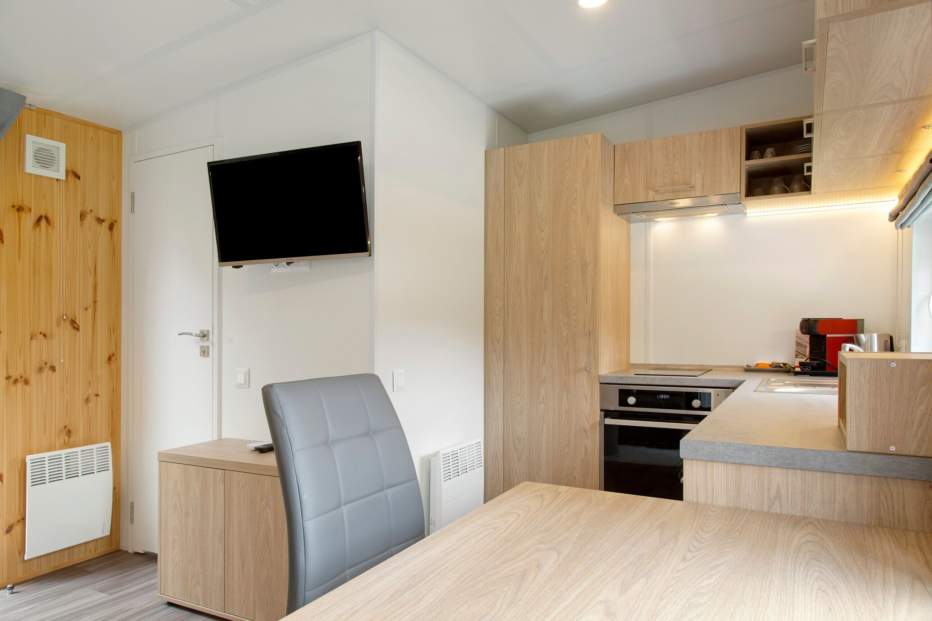 Une petite cuisine équipée avec une cuisinière, un four à micro-ondes et un téléviseur à écran plat fixé au-dessus du plan de travail.