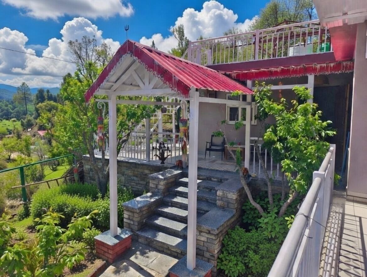 A two-story building with a red roof, a balcony with a railing, and a stone staircase leading to a covered area.