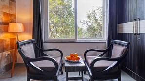 A room with two chairs, a table with fruit, a lamp, and a window with a view of trees. - Panoramic Views 4-bedroom Luxury villa in marvelous Mukteshwar for your getaway (Mukteshwar)