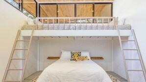 A bunk bed with a wooden ladder, white bedding, and a patterned pillow.