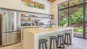 A modern kitchen with a large island, stainless steel appliances, and a view of the garden.
