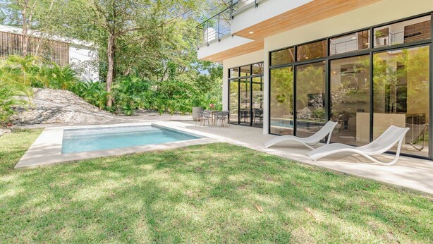 A modern house with a swimming pool, outdoor seating, and a view of the surrounding garden.