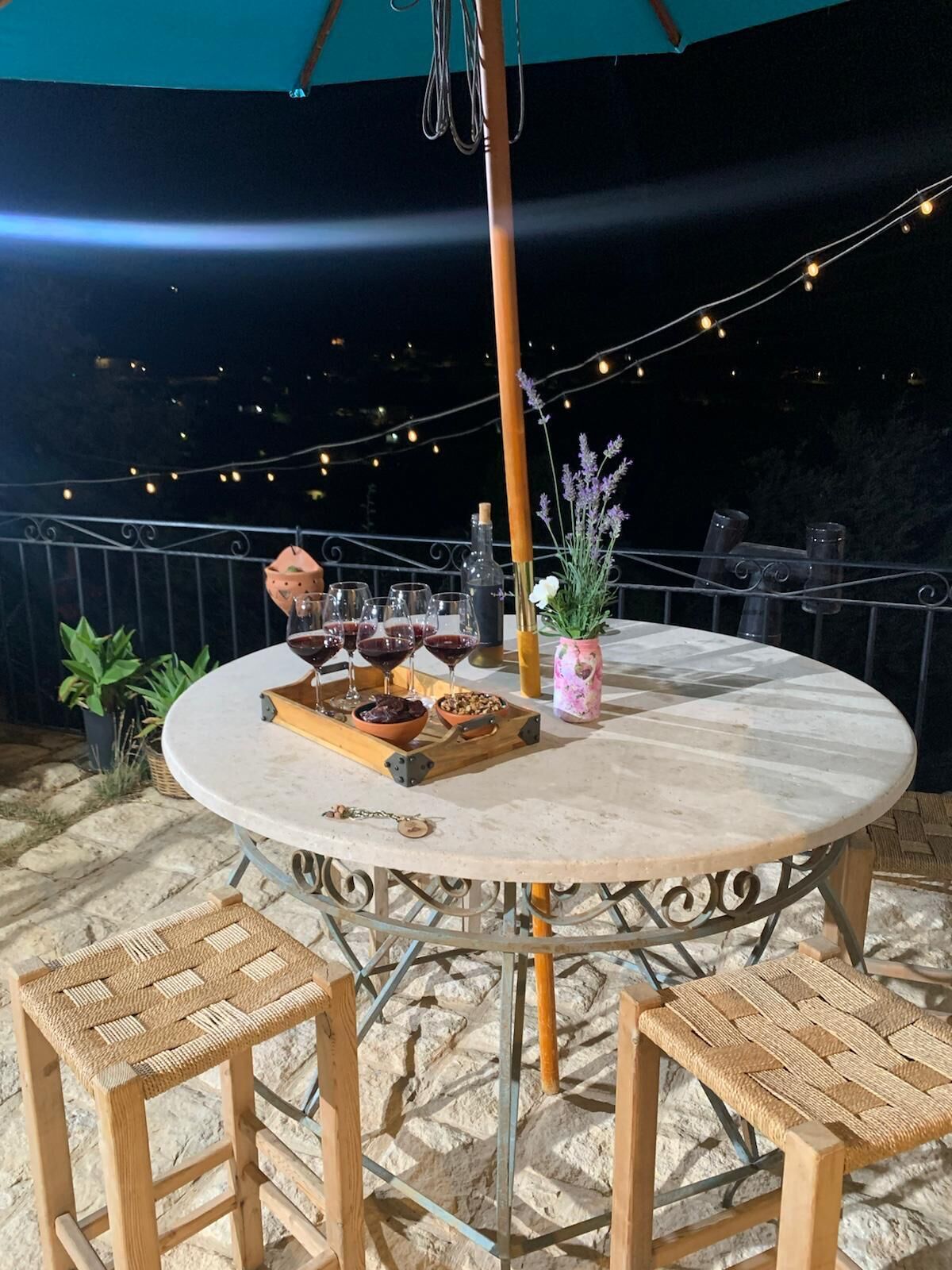 Un espace de restauration en plein air avec une table ronde, quatre chaises en osier, une bouteille, un bol et un vase rempli de fleurs.