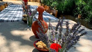 Un área de comedor al aire libre con mantel a cuadros, una jarra de terracota grande y un florero de vidrio con lavanda y flores rojas.