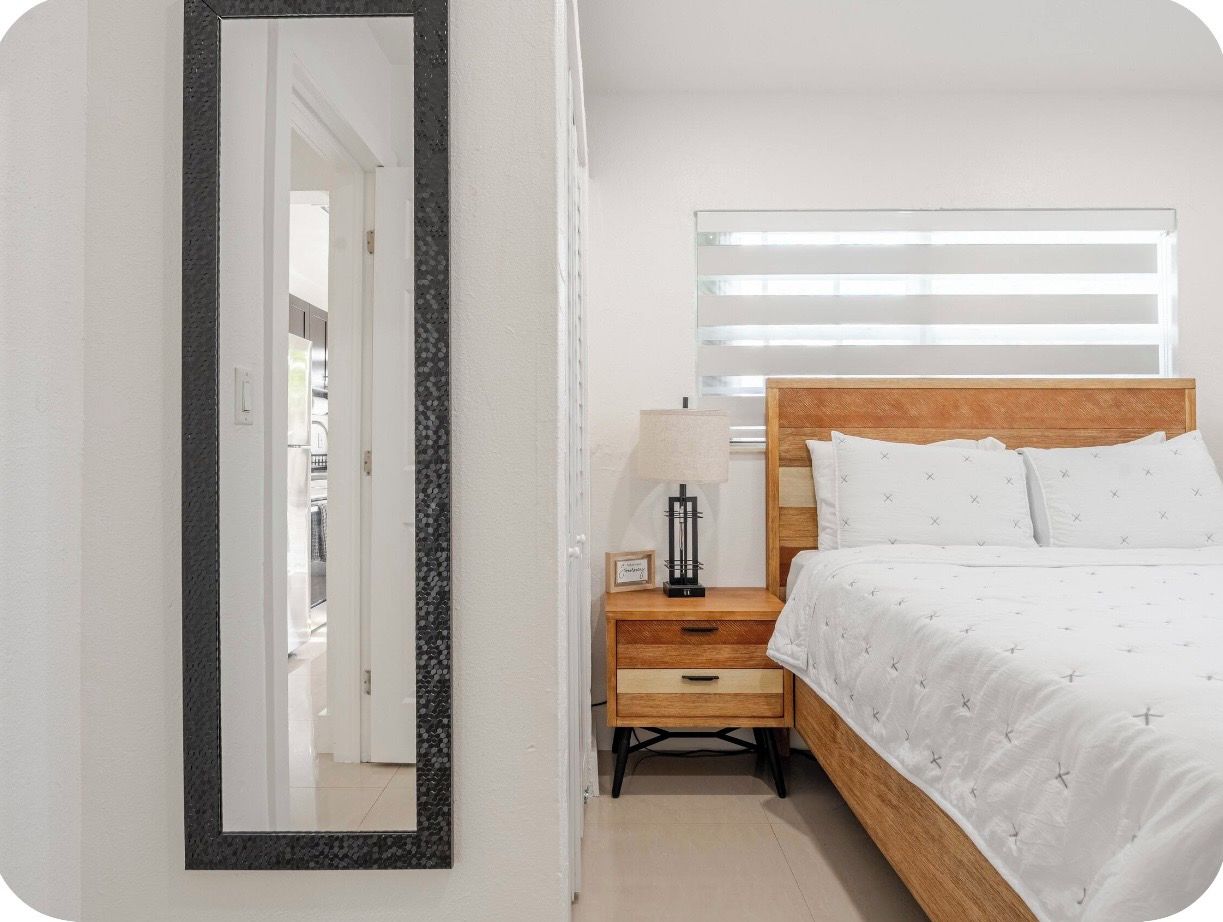 A bedroom with a bed, bedside table, lamp, and a mirror.