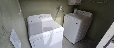 A laundry room with two white washing machines, a wall-mounted heater, and a power outlet.