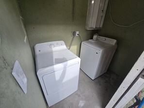 A laundry room with two white washing machines, a wall-mounted heater, and a power outlet. - Miami Health District 1/1 w/2Gbps WiFi Stainless Steel 75” & 55” TV Pet friendly (Miami)