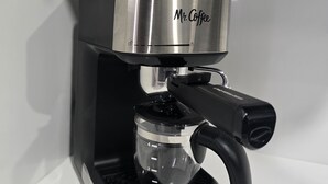 Eine Kaffeemaschine mit transparentem Wasserbehälter und einem schwarzen Griff.