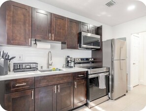 A modern kitchen with dark wooden cabinets, stainless steel appliances, and a white countertop. - Miami Health District 1/1 w/2Gbps WiFi Stainless Steel 75” & 55” TV Pet friendly (Miami)