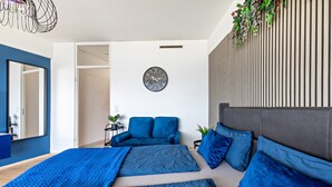 Ein modernes Schlafzimmer mit einem großen Bett, einer Couch, einer Wanduhr und einer Pflanze.