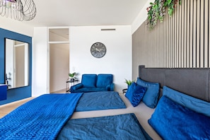 Un dormitorio moderno con una cama grande, un sofá, un reloj en la pared y una planta.