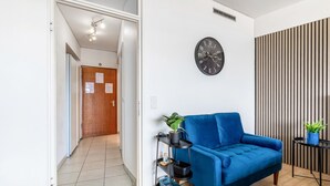 Ein modernes Wohnzimmer mit einem blauen Sofa, einer schwarzen Uhr an der Wand, einem schwarzen Regal mit Pflanzen und einer gestreiften Wandverkleidung.