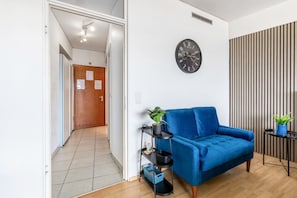 Una sala de estar moderna con un sofá azul, un reloj negro en la pared, una estantería negra con plantas y un panel de pared a rayas.