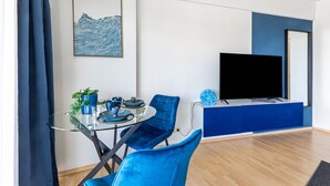 Ein modernes Wohnzimmer mit einem Glastisch, blauen Stühlen, einem Flachbildfernseher und einer blau gestrichenen Wand.