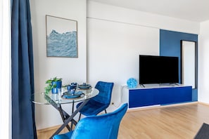 Una sala de estar moderna con una mesa de comedor de cristal, sillas azules, un televisor de pantalla plana y una pared de acento en tono azul.