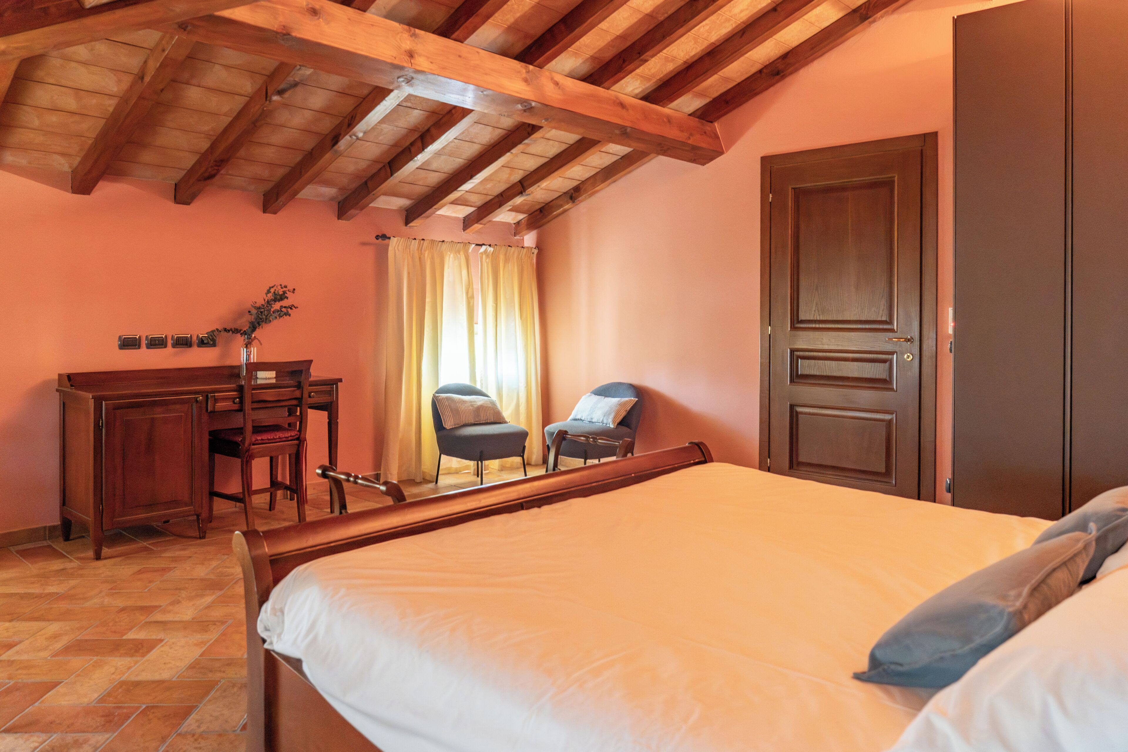 Un dormitorio con techo de madera, una cama, un escritorio, dos sillas y un armario.