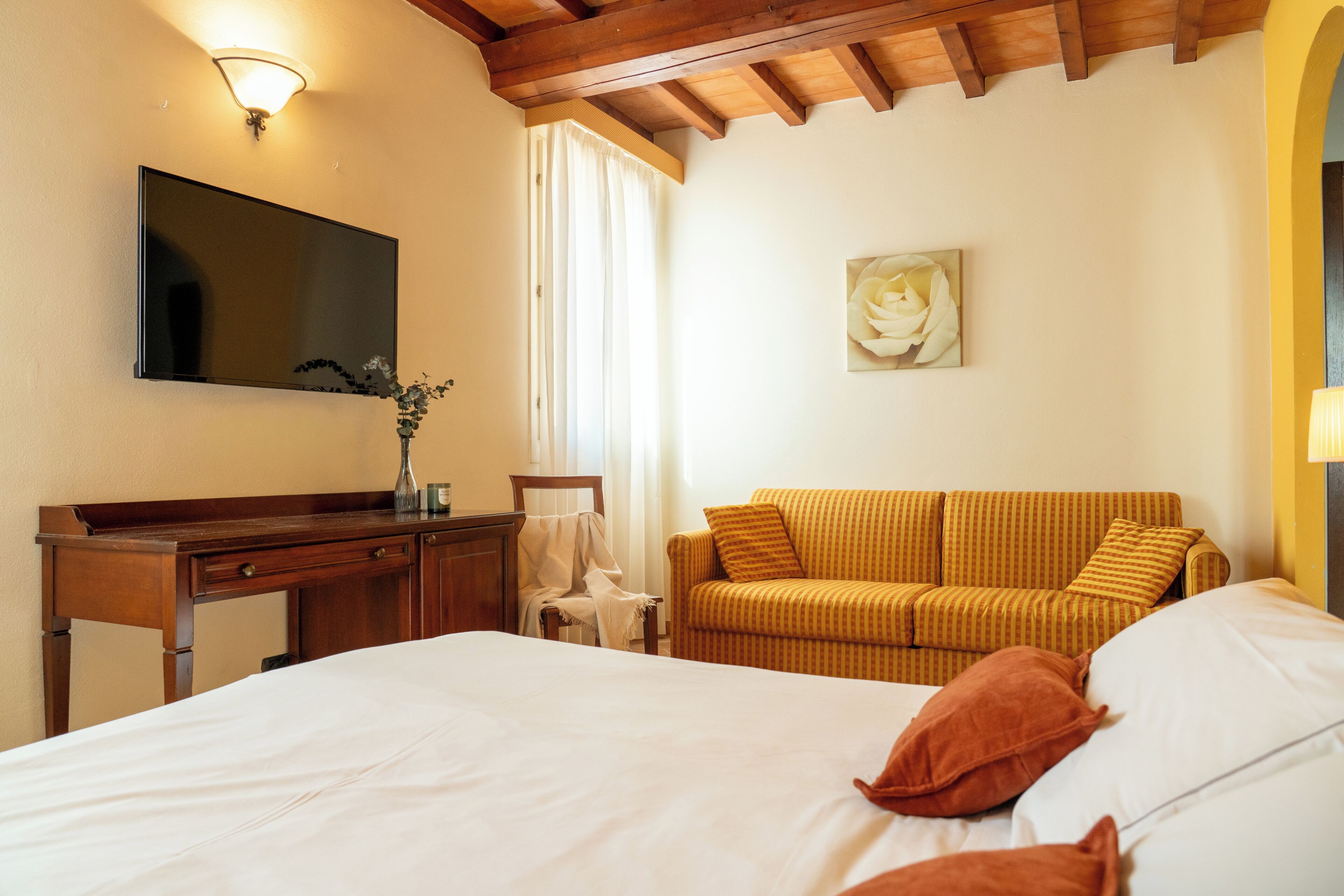A hotel room with a bed, a sofa, a desk, a TV, and a painting.