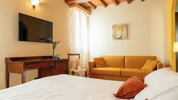 A hotel room with a bed, a sofa, a desk, a TV, and a painting.