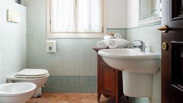 A bathroom with a toilet, bidet, sink, and a window with curtains.
