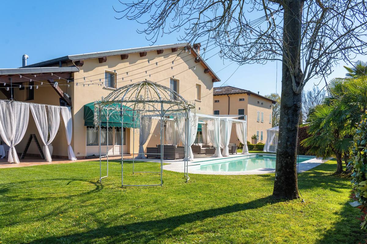 A house with a swimming pool, a covered outdoor seating area, and a lawn.