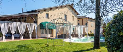 A house with a swimming pool, a covered outdoor seating area, and a lawn.