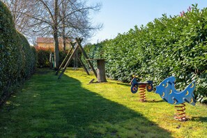 A grassy area with a swing set, a bird-shaped play structure, and a hedge.