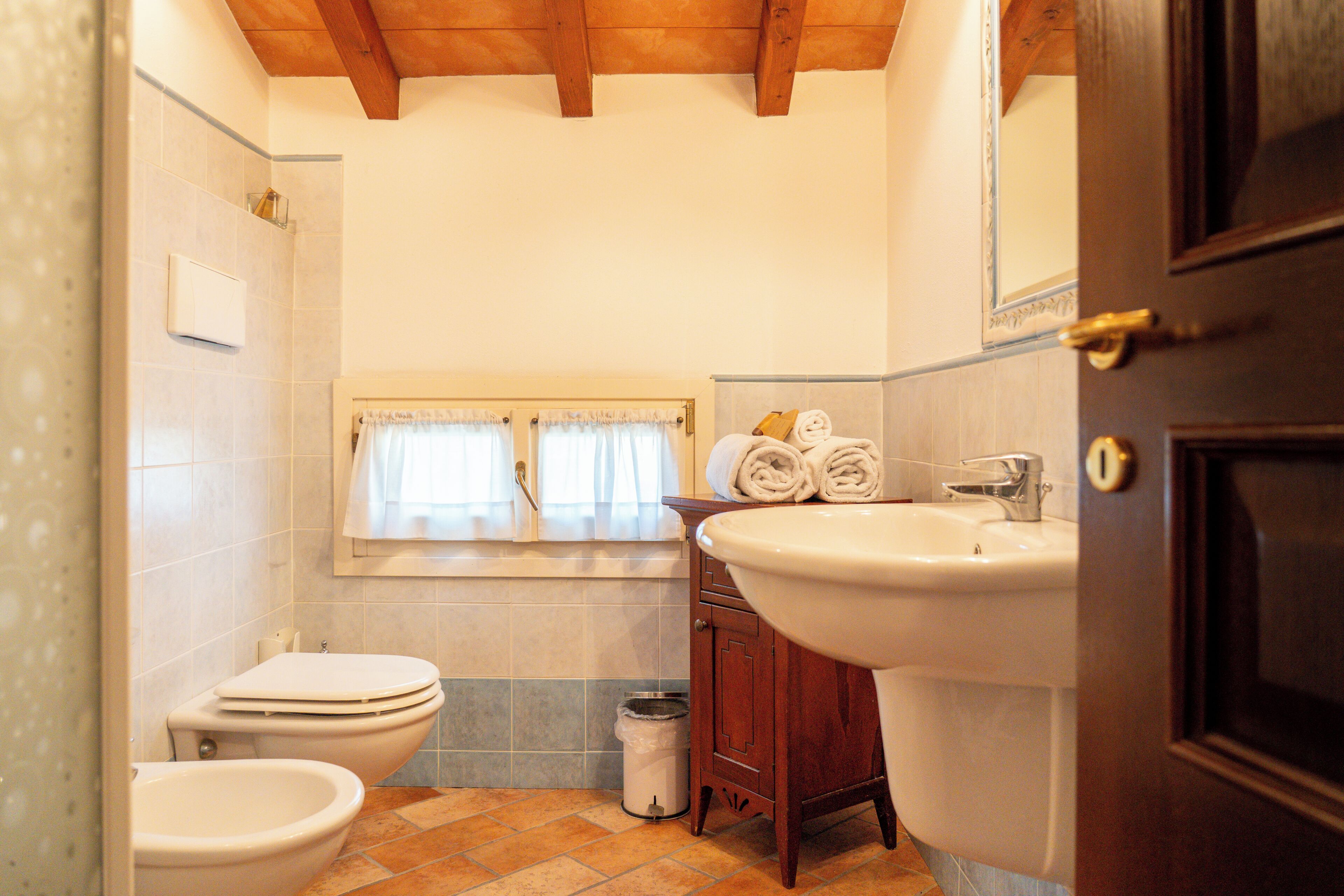 Un baño con inodoro, bidé, lavabo y ventana con cortinas.