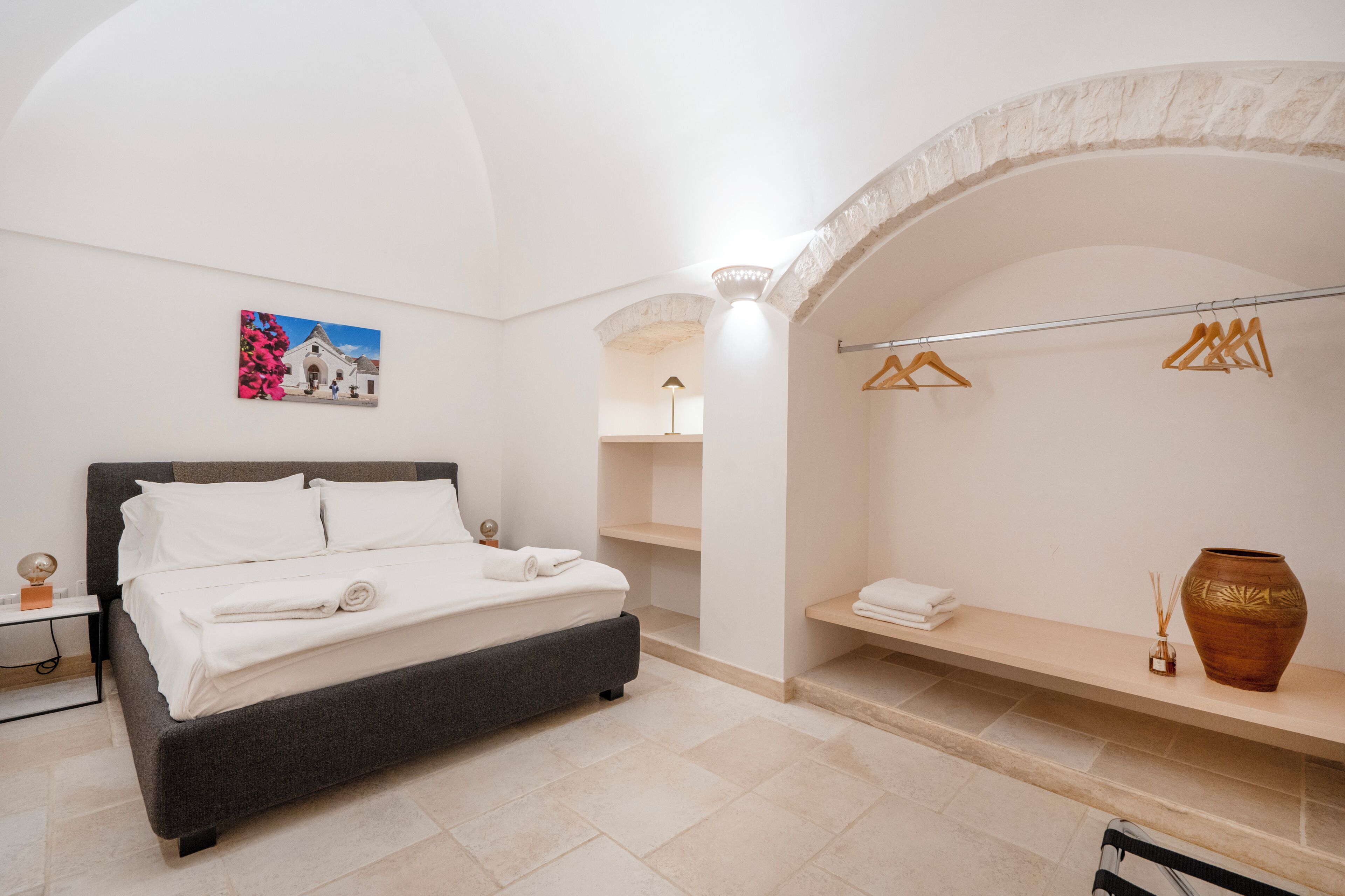 Une chambre à coucher moderne avec un lit, une étagère fixée au mur, un portant à vêtements et un vase décoratif.