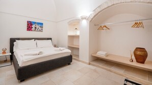 A modern bedroom with a bed, a wall-mounted shelf, a hanging clothes rack, and a decorative vase. - Trullo in Alberobello apartment for 4/6 people (Alberobello)