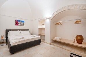 A modern bedroom with a bed, a wall-mounted shelf, a hanging clothes rack, and a decorative vase. - Trullo in Alberobello apartment for 4/6 people (Alberobello)