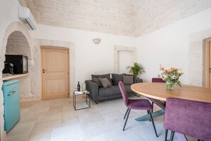 A modern living room with a grey sofa, purple chairs, a wooden dining table, and a small kitchen area with a fridge and microwave. - Trullo in Alberobello apartment for 4/6 people (Alberobello)