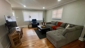 Un salon avec un canapé gris, un fauteuil noir, une table basse en bois et un téléviseur posé sur un meuble.